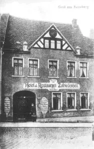 Hier ist ein recht altes schwarz-weiß Foto zu sehen, aus den Zeiten, als der Gasthof Zufriedenheit erstmal namentlich erwähnt wurde, der Schriftzug auf der Hausfassade lautet „Hotel & Restaurant Zufriedenheit“, darüber ist noch die Fernruf Nummer aufgeführt.