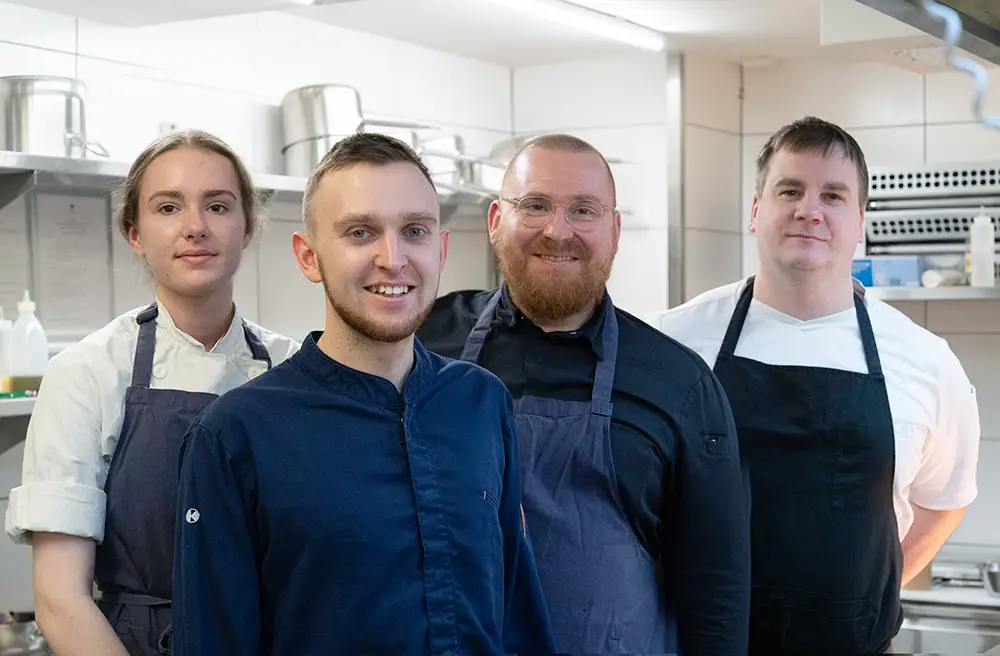 Drei junge, dynamische Köche und eine Köchin, die nebeneinanderstehen und Tatendrang vermitteln.